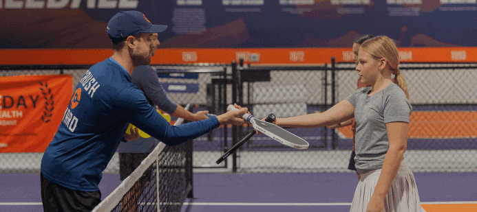 A coach and player tapping paddles across the net
