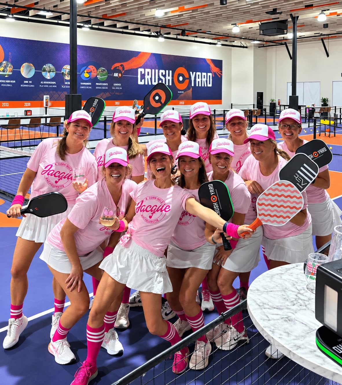 Friends celebrating at Crush Yard in matching pink outfits, with drinks and paddles